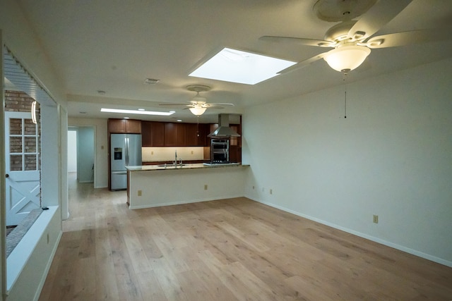 kitchen featuring wall chimney exhaust hood, stainless steel fridge, kitchen peninsula, and light hardwood / wood-style flooring