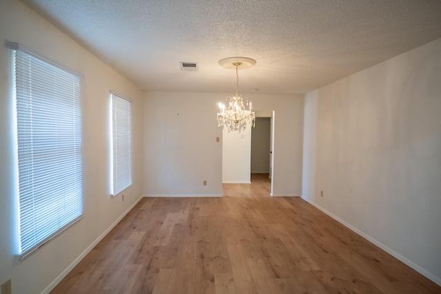 unfurnished dining area with a chandelier, a textured ceiling, and light hardwood / wood-style flooring