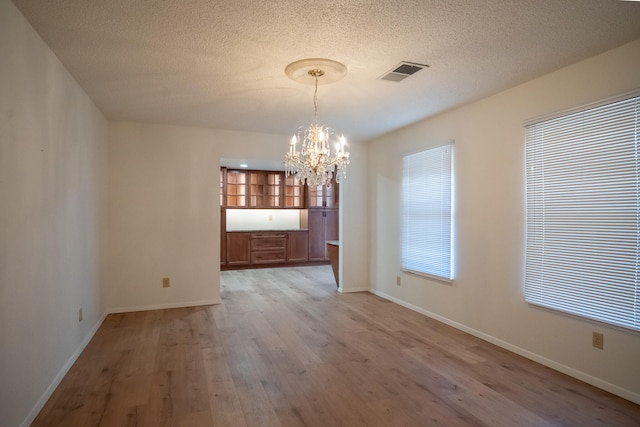 unfurnished dining area with hardwood / wood-style floors, a textured ceiling, and an inviting chandelier