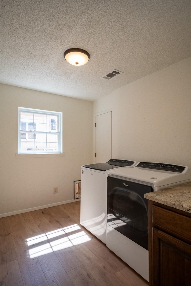 washroom featuring washing machine and clothes dryer, light hardwood / wood-style flooring, cabinets, and a textured ceiling