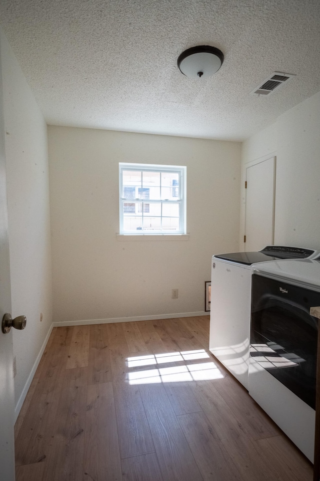 laundry area featuring light hardwood / wood-style flooring, washer and dryer, and a textured ceiling