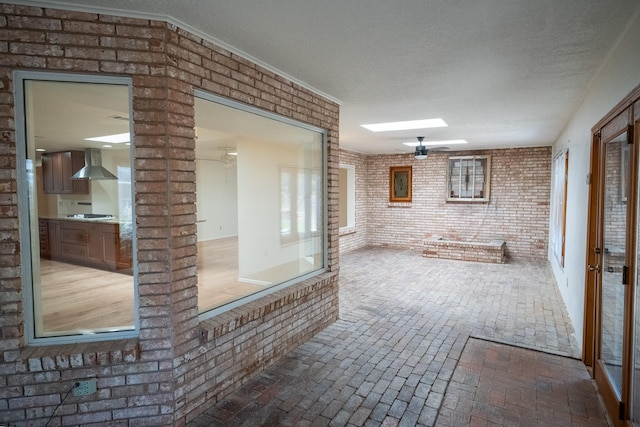 interior space featuring a skylight, ornate columns, ornamental molding, a textured ceiling, and brick wall