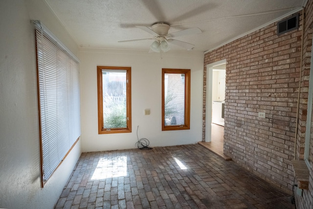 unfurnished room featuring ceiling fan, brick wall, and a textured ceiling