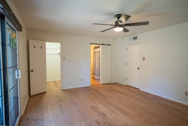 unfurnished bedroom with light wood-type flooring, ensuite bath, a textured ceiling, ceiling fan, and a closet