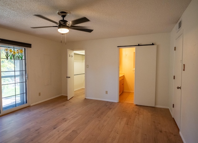 unfurnished bedroom with a barn door, ensuite bathroom, light hardwood / wood-style flooring, and ceiling fan