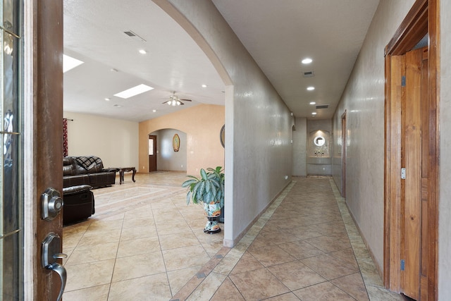 hallway with lofted ceiling with skylight, light tile patterned floors, recessed lighting, and arched walkways