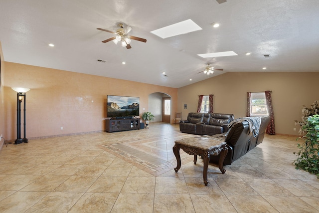 tiled living room with ceiling fan and vaulted ceiling with skylight