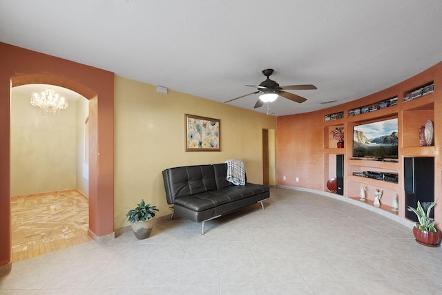 sitting room with built in shelves, tile patterned flooring, and ceiling fan with notable chandelier