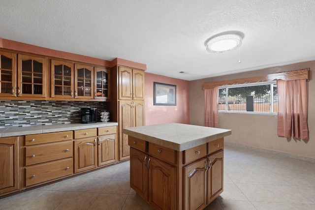 kitchen featuring a textured ceiling, a center island, tile counters, backsplash, and light tile patterned flooring