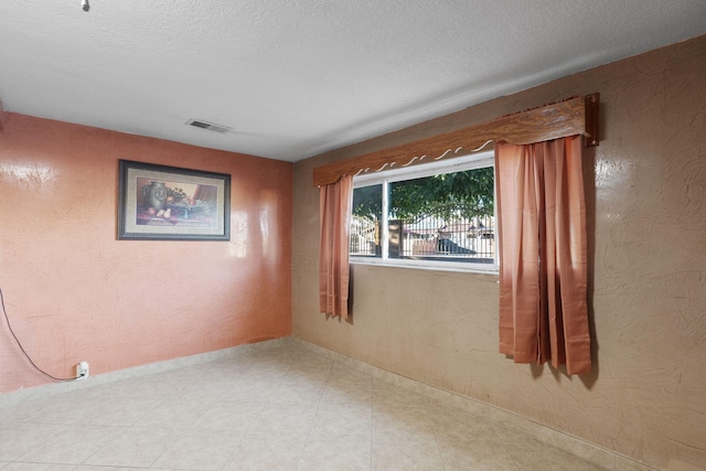 empty room featuring a textured wall, visible vents, and a textured ceiling