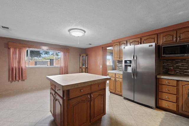 kitchen featuring tasteful backsplash, a kitchen island, light tile patterned flooring, stainless steel appliances, and tile counters