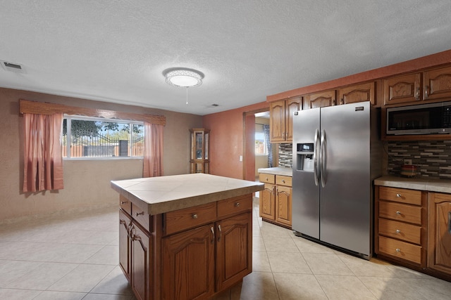 kitchen with visible vents, tile countertops, brown cabinets, light tile patterned flooring, and stainless steel appliances