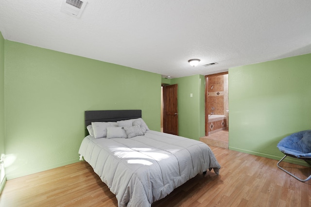 bedroom with light wood-type flooring, connected bathroom, and a textured ceiling