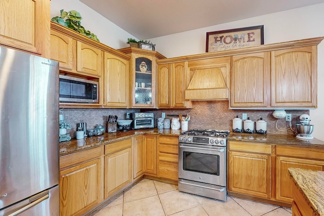 kitchen with dark stone countertops, backsplash, stainless steel appliances, and premium range hood