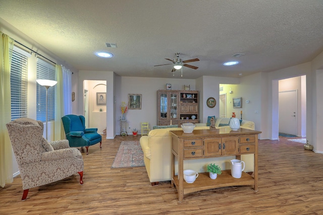 living room with a textured ceiling, ceiling fan, and wood-type flooring