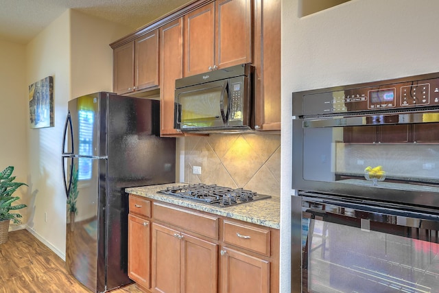 kitchen with black appliances, backsplash, light stone countertops, and hardwood / wood-style floors