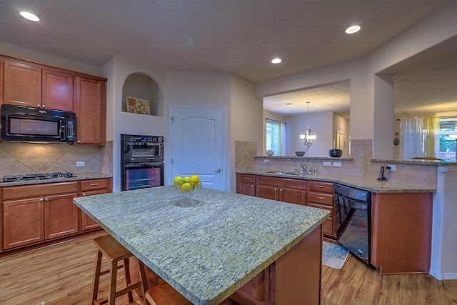 kitchen featuring backsplash, black appliances, kitchen peninsula, light wood-type flooring, and a breakfast bar area