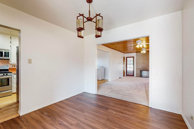 interior space featuring hardwood / wood-style floors, ceiling fan with notable chandelier, washer / dryer, and a fireplace