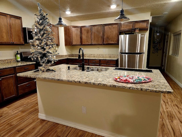 kitchen with sink, an island with sink, stainless steel refrigerator, and decorative light fixtures