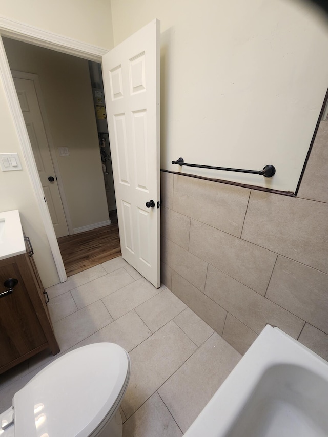 bathroom featuring tile patterned floors, tile walls, a tub, toilet, and vanity