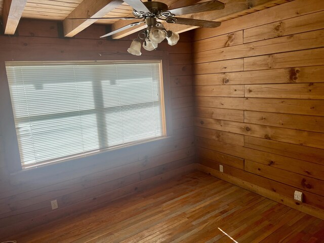 spare room with wood walls, beamed ceiling, wood-type flooring, ceiling fan, and wood ceiling