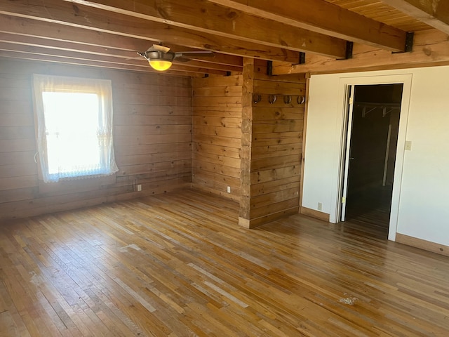 unfurnished room with wood walls, beamed ceiling, wood-type flooring, and baseboards