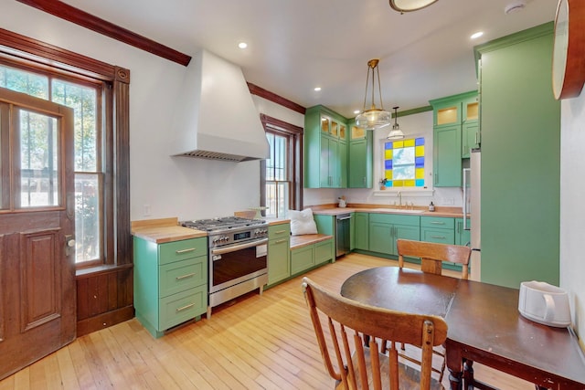 kitchen with premium range hood, crown molding, stainless steel appliances, pendant lighting, and light hardwood / wood-style floors