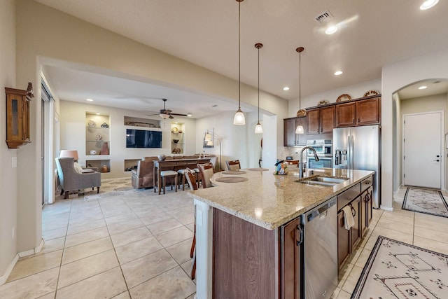 kitchen featuring a kitchen island with sink, sink, light stone countertops, decorative light fixtures, and appliances with stainless steel finishes