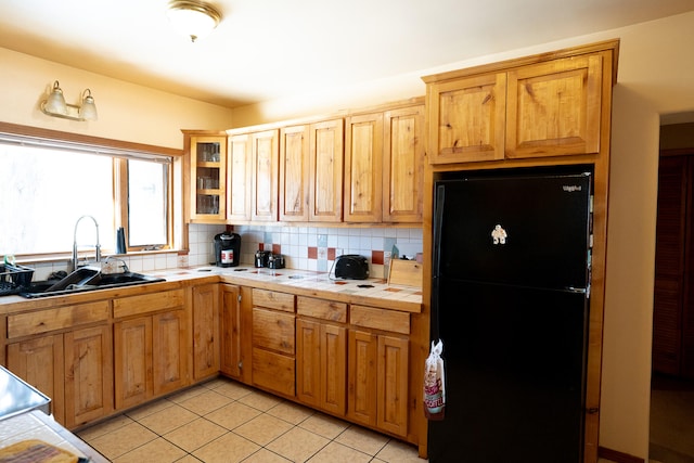 kitchen with tile countertops, sink, tasteful backsplash, light tile patterned floors, and black refrigerator