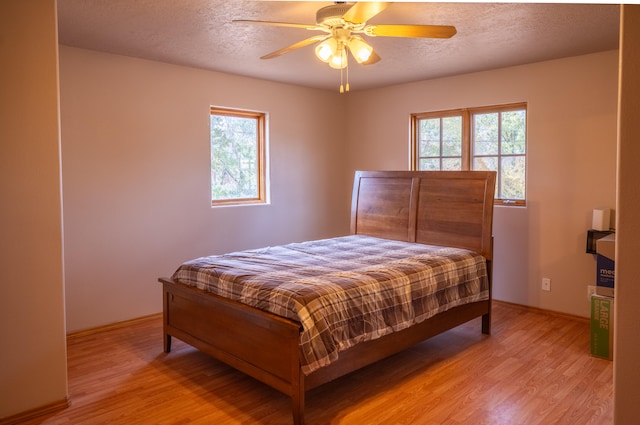 bedroom featuring multiple windows, a textured ceiling, ceiling fan, and light hardwood / wood-style flooring