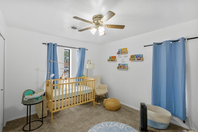 bedroom featuring a textured ceiling, carpet, a nursery area, and ceiling fan