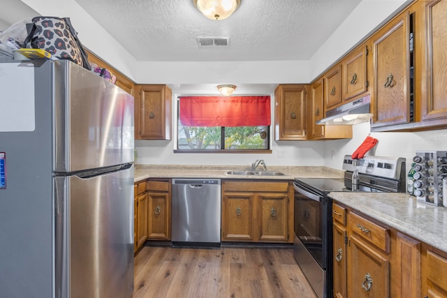 kitchen featuring a textured ceiling, appliances with stainless steel finishes, sink, and light hardwood / wood-style flooring