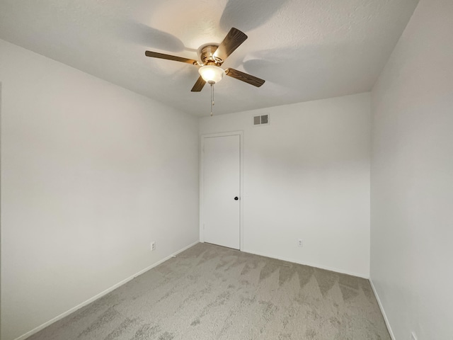 spare room featuring ceiling fan, light colored carpet, and a textured ceiling