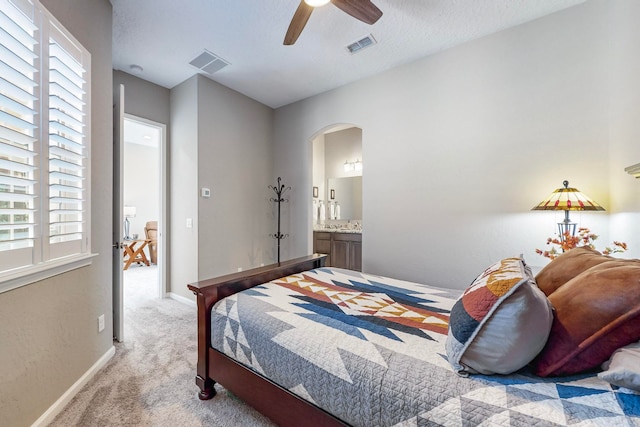 bedroom featuring multiple windows, light colored carpet, ceiling fan, and ensuite bathroom