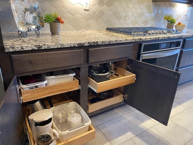 kitchen featuring backsplash, appliances with stainless steel finishes, light tile patterned floors, and light stone countertops