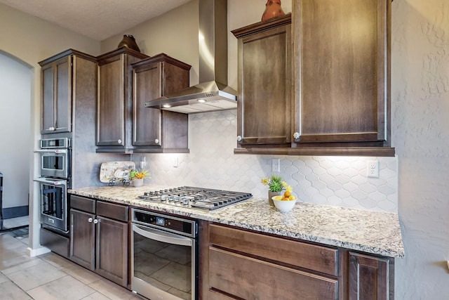 kitchen with light stone countertops, wall chimney exhaust hood, appliances with stainless steel finishes, and tasteful backsplash