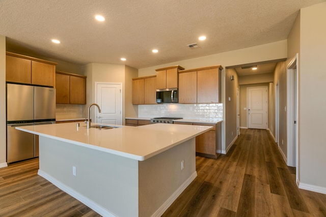 kitchen featuring a center island with sink, sink, backsplash, dark hardwood / wood-style floors, and stainless steel appliances