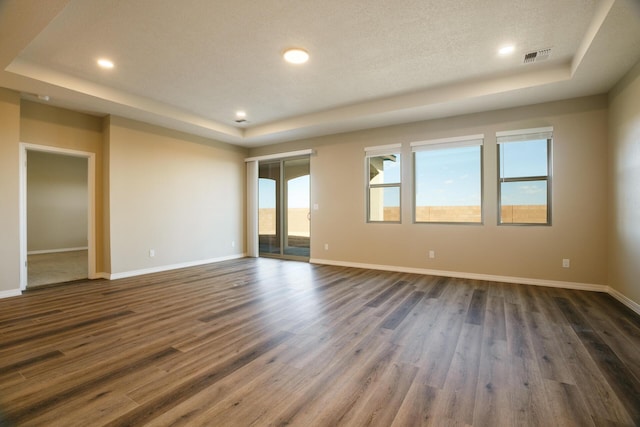 empty room featuring dark wood-type flooring, a raised ceiling, and a textured ceiling