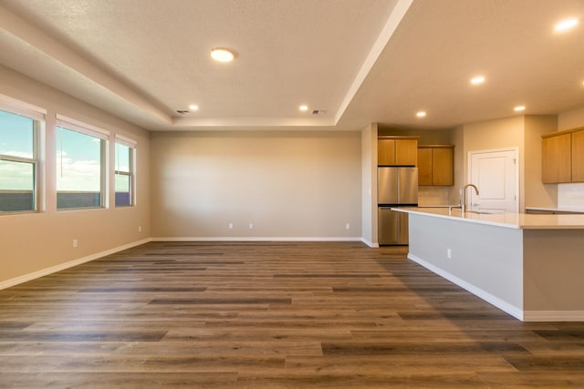 unfurnished living room featuring sink, dark wood-type flooring, a textured ceiling, and a raised ceiling