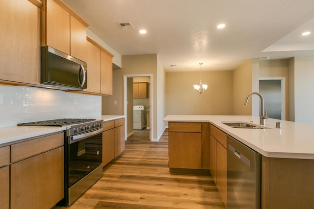 kitchen with sink, washer / dryer, stainless steel appliances, and an island with sink