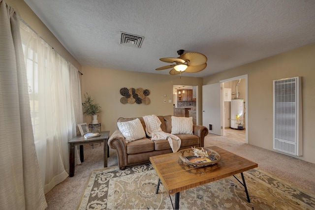 living room with water heater, ceiling fan, light carpet, and a textured ceiling