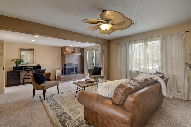 carpeted living room with a textured ceiling, ceiling fan, and a tiled fireplace