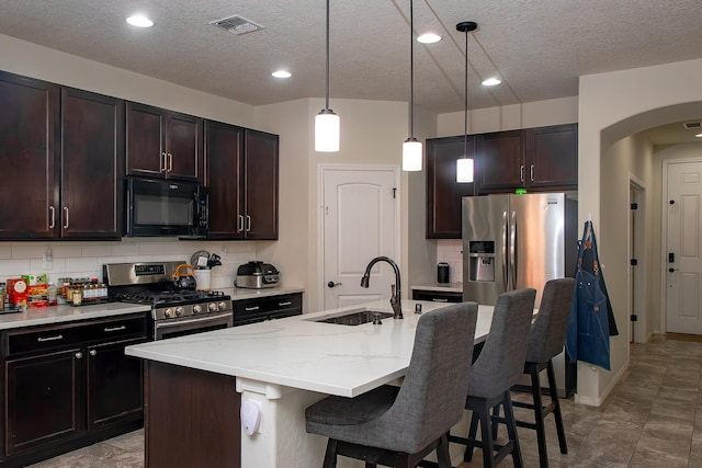 kitchen with pendant lighting, stainless steel appliances, sink, and an island with sink