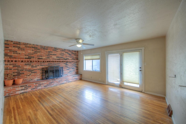 unfurnished living room with ceiling fan, light wood-type flooring, a fireplace, and a textured ceiling