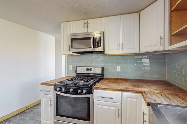 kitchen with wooden counters, white cabinetry, backsplash, and appliances with stainless steel finishes