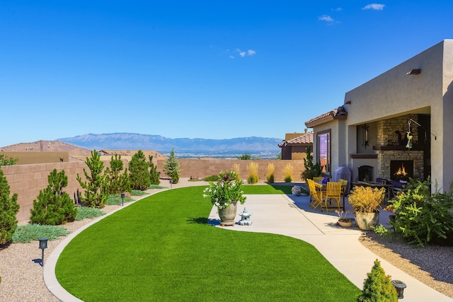 view of yard featuring a lit fireplace, a patio, a fenced backyard, and a mountain view