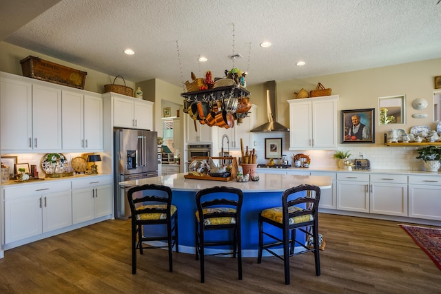 kitchen featuring a kitchen bar, white cabinetry, a kitchen island with sink, wall chimney range hood, and backsplash