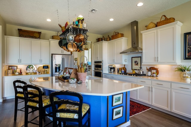 kitchen with white cabinets, wall chimney range hood, a center island with sink, a breakfast bar area, and stainless steel appliances