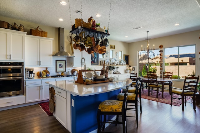 kitchen with wall chimney range hood, a center island, stainless steel double oven, and white cabinetry