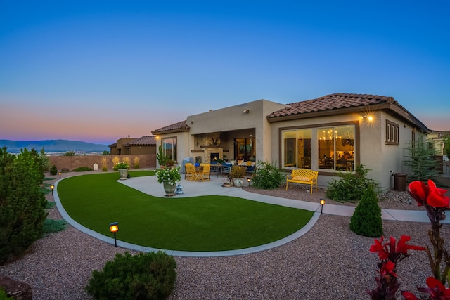 back house at dusk with a patio area and a lawn